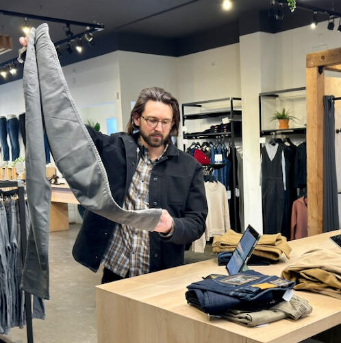 Man holds up a pair of DUER jeans for inspection.
