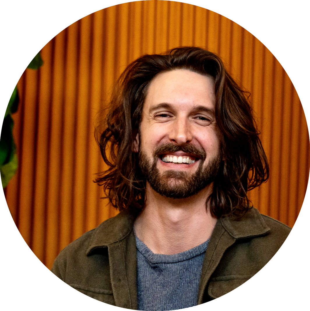 Devon de Balasi Brown with long hair in front of an orange background.